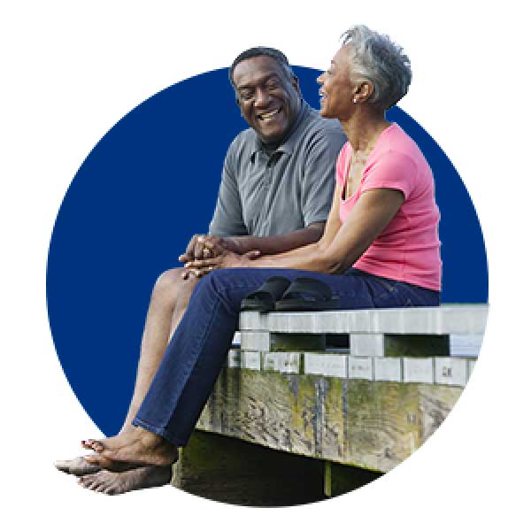smiling couple sitting barefoot on edge of a dock